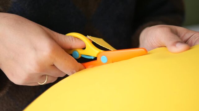 Person uses scissors to cut yellow paper on a flat surface