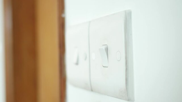 Finger pressing a light switch on a wall, turning power on or off