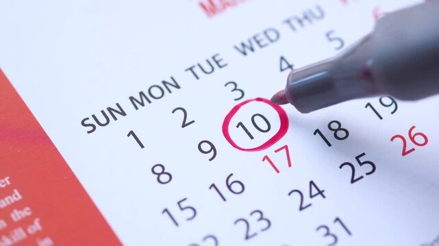 Close up view of hand circling date number ten on calendar with red marker pen