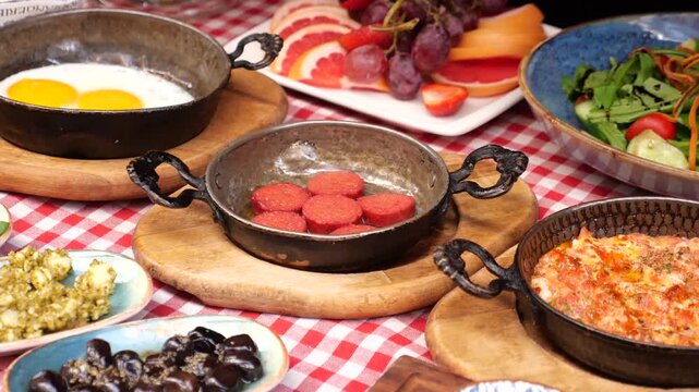 Traditional turkish breakfast spread with sizzling eggs sucuk and fresh salad on checkered tablecloth