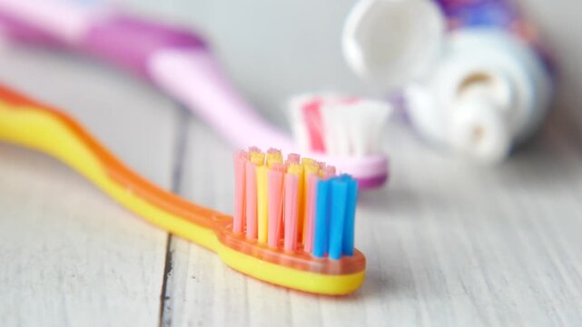 A close up view of several colorful toothbrushes and an open tube of toothpaste on a wooden surface, highlighting dental hygiene tools in a bright, clean setting with a dynamic focus pull