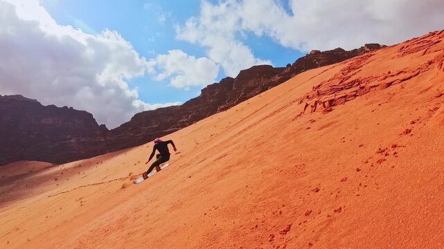 Male caucasian beginner learning solo sandboarding sports on steep red dune in Wadi rum with struggle balance challenge and failed attempts adventure concept Jordan. Practise makes perfect