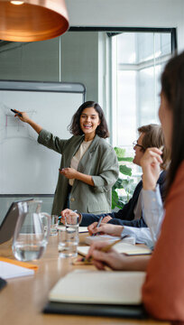 Enthusiastic female hardware engineer celebrating a breakthrough moment by looking directly at the camera while sketching a product prototype diagram for her team.