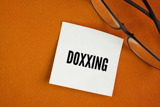 Glasses and paper with the word DOXXING. publish private or identifying information about a particular individual on the internet, typically with malicious intent.