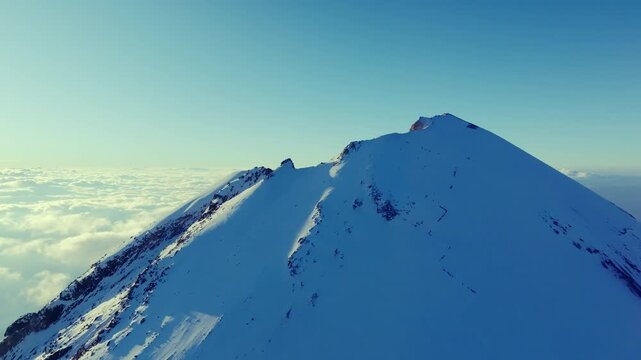 4K aerial drone view of the snow covered summit of Pico de Orizaba, also known as Citlaltepetl, the highest volcano in Mexico. Dramatic volcanic peak rising above a sea of clouds.