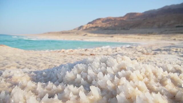 Close up Dead Sea salt crystals on shoreline beach in Jordan at sunset with turquoise water desert coast lowest point on Earth landscape. Jordan - Israel border line zone