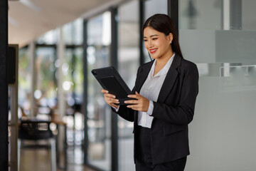 Obraz premium A cheerful businesswoman engages with her tablet in a sleek, modern office setup, representing a fusion of technology and professionalism, perfect for contemporary workplace themes.