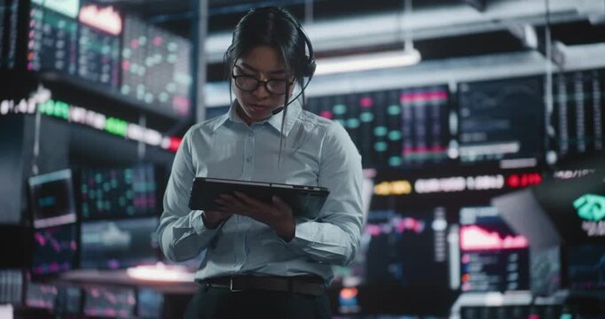 Professional Woman Stands Before Quad Monitor Setup, Holding Digital Tablet Monitor Real Time Stock Indices. Girl Steps Forward Input Data on Keyboard. Active Management and Leadership in Finance Hub.