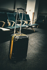 Black suitcase with yellow accents sits in an empty airport waiting area © Tom Harwood