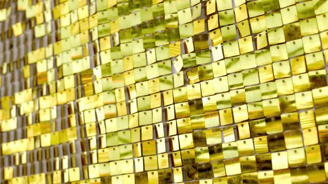Panning shot of gold sequin curtain shifting and catching light reflections across textured metallic surface in close up studio setting