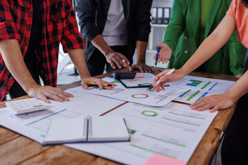 A group of professionals engaged in a teamwork session, discussing detailed reports and business metrics while analyzing performance data on a wooden table. © David