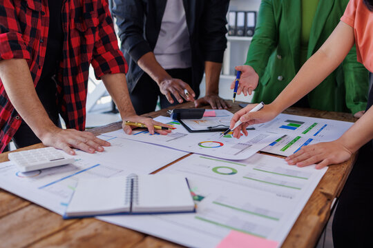 A group of professionals engaged in a teamwork session, discussing detailed reports and business metrics while analyzing performance data on a wooden table.