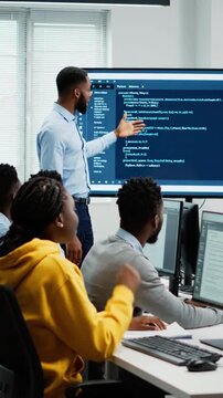 Instructor teaches programming concepts to students in a classroom setting with large display screen