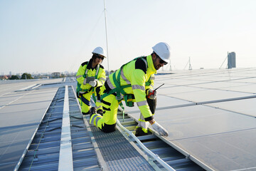 Professional technicians in safety gear inspecting solar panels on a commercial rooftop. Maintenance workers using a tablet and walkie-talkie for green energy system installation.