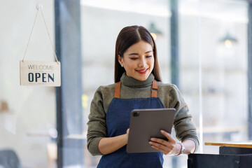 Fototapeta premium This image displays a joyful woman in an apron holding a tablet, exuding warmth and approachability in a retail setting with an open sign prominently displayed.