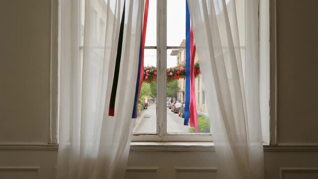 Window with sheer white curtains and colorful ribbons revealing old building