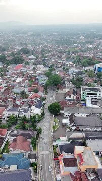 Aerial drone view of a dense urban neighborhood with red rooftops, a central road, and scattered trees stretching toward a hazy horizon, capturing the atmosphere of a busy Southeast Asian city