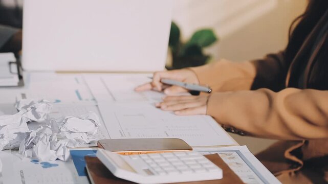 Accountant reviewing printed financial reports at messy office desk with calculator and sticky notes under soft window daylight for audit and corporate finance work