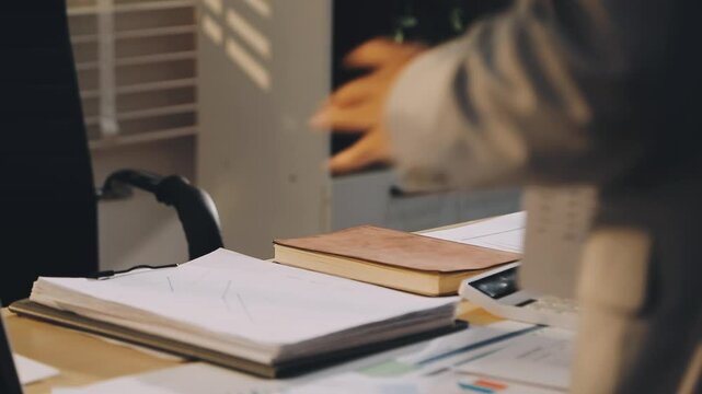 Accountant reviewing printed financial reports at messy office desk with calculator and sticky notes under soft window daylight for audit and corporate finance work