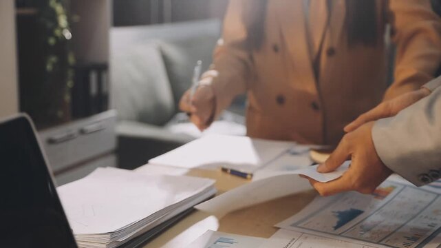 Accountant reviewing printed financial reports at messy office desk with calculator and sticky notes under soft window daylight for audit and corporate finance work
