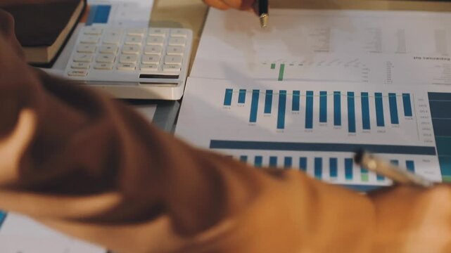 Accountant reviewing printed financial reports at messy office desk with calculator and sticky notes under soft window daylight for audit and corporate finance work