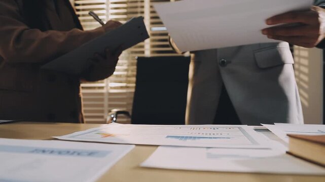 Accountant reviewing printed financial reports at messy office desk with calculator and sticky notes under soft window daylight for audit and corporate finance work