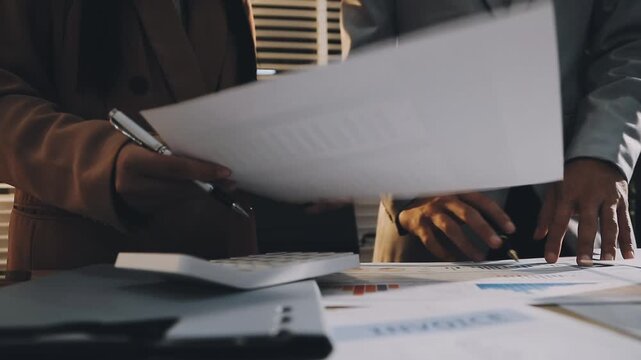 Accountant reviewing printed financial reports at messy office desk with calculator and sticky notes under soft window daylight for audit and corporate finance work