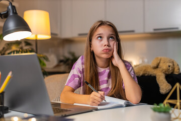 Teenager girl at night home works on homework feels tired writes notes stays focused. Caucasian...