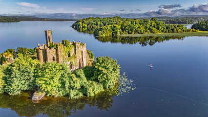 Aerial drone view of woman paddling SUP board on beautiful Lough Key lake with McDermotts Castle on small island, stand up paddling water adventure on vacation, travel in Ireland