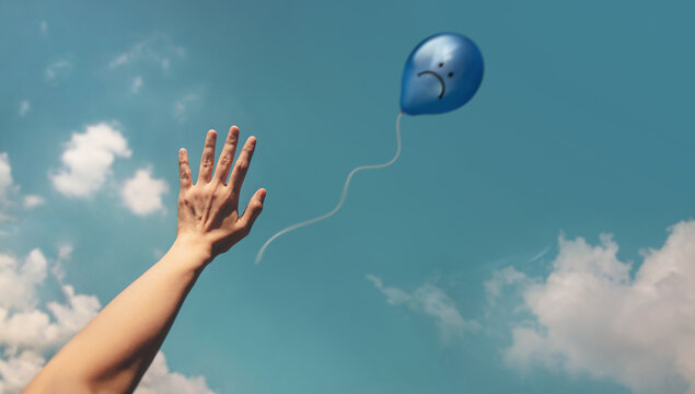 Mind, Mental Health. Hand releasing Blue Sadness Balloon to sky