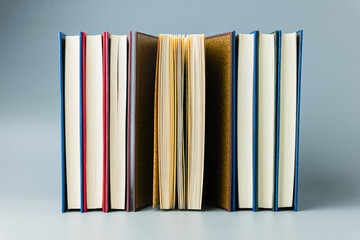 Row of colorful hardcover books with one open book in the center on minimal background