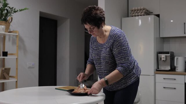 Senior woman seasoning minced meat in the kitchen