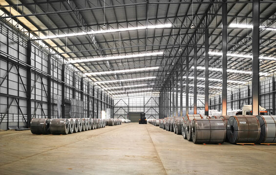 Interior view of a massive industrial warehouse storing rows of large steel coils for manufacturing and distribution.