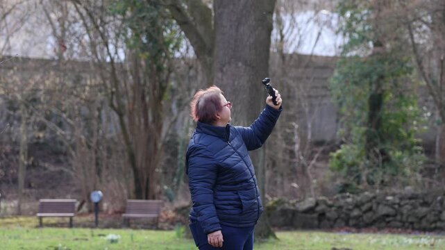 Woman taking photos or videos outside in the park with a camera