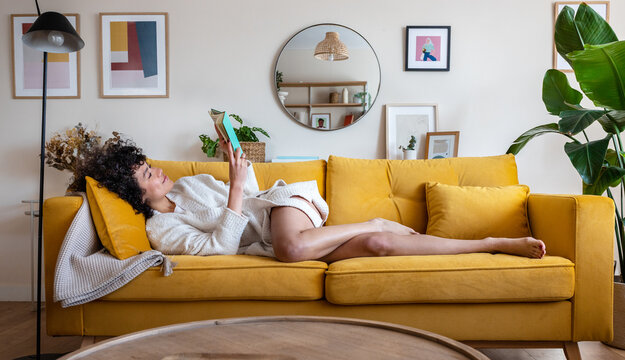 Woman relaxing on yellow sofa reading book