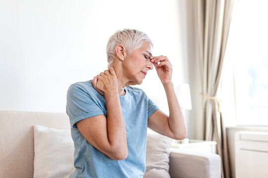 Sinus pain. Mature woman with headache, people with body-muscles problem, healthcare and medicine concept. Elderly lady sitting on the sofa and holding painful face and neck with hands. Flu symptoms.