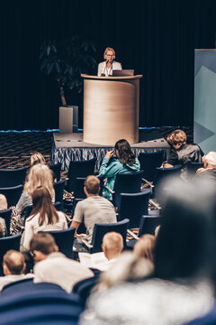 Female speaker giving a talk on corporate business conference. Unrecognizable people in audience at conference hall. Business and Entrepreneurship event
