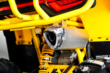 Close up of a silver exhaust pipe on a yellow powerful all terrain vehicle atv quad bike with visible suspension and tire for off road racing outdoors © Tatiana