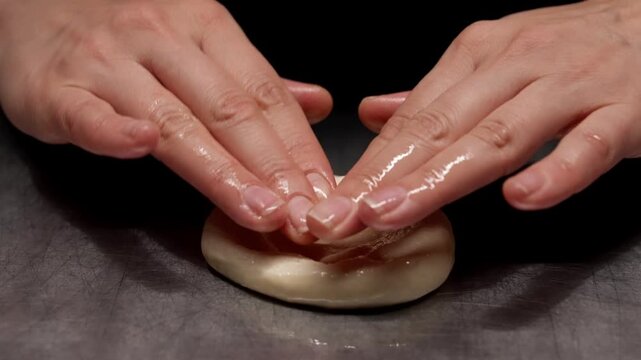 Closeup sequence of soft dough being shaped and gently flattened by hands on a metal surface, highlighting texture, elasticity, and preparation stages in baking