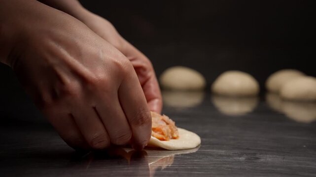 Close-up sequence of hands shaping stuffed dough on a reflective metal surface, folding and sealing savory filling inside delicate pastry for baking