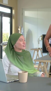 Vertical video: Hearing peer talking in office, she in green hijab gesturing at laptop, copy space