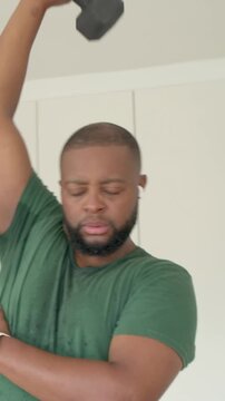 Vertical video: Starting man doing overhead triceps extension for workout at home, holding dumbbell