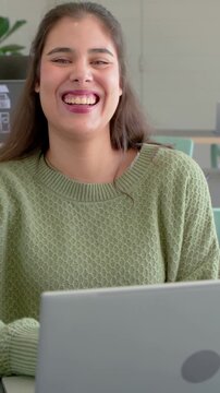 Office worker viewing laptop and shifting smile into open laughter while reacting to funny chat