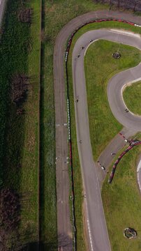 Karting Track from Above: An aerial view of a winding karting track with a few karts racing, surrounded by green grass and trees, capturing the thrill of speed and competition. Milan, Italy