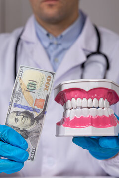 Un dentiste qui tient un mod&egrave;le 3D de dentier et de l'argent, signifiant les frais dentaires. Le format est vertical.