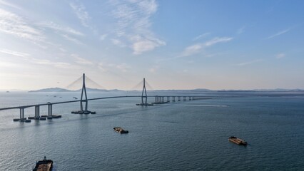 Fototapeta premium Wide-angle aerial drone view of the Incheon Bridge, South Korea's longest cable-stayed bridge, stretching across the sea under a soft blue sky with scattered clouds.