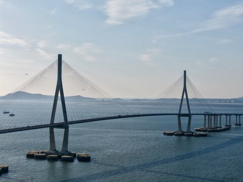 Majestic aerial view of the Incheon Bridge's massive cable-stayed pylons, captured with a telephoto lens to emphasize the grand architectural scale and structural detail over the sea.