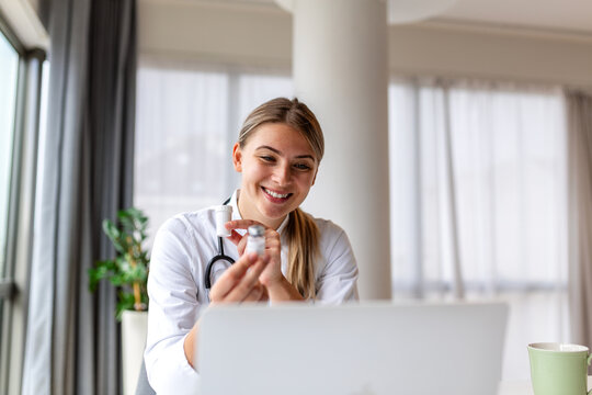 Female doctor showing medicine bottles during online medical consultation. Telehealth and pharmacy concept. Healthcare professional explaining prescription or vaccine via video call on laptop.