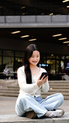 Fototapeta premium asian woman college student holding and looking smartphone walking in campus