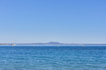 Open view across calm Mediterranean water toward distant mountains on the horizon near the coast of Mallorca, Spain, with a small sailboat and navigation buoys visible offshore.